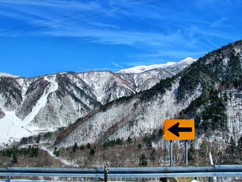 Road sign by snowcapped mountains against sky