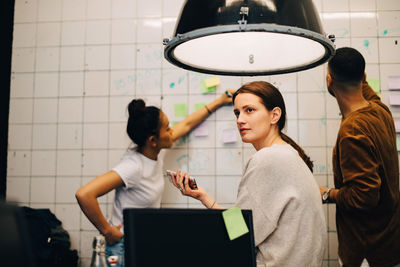 Young businesswoman looking away while hackers planning over wall at small office