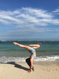 Full length of woman doing handstand on shore at beach against sky