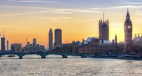 Westminster bridge over thames river by big ben against sky during sunset