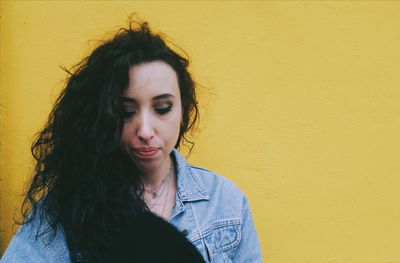 Close-up of beautiful young woman against yellow wall