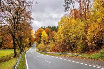 Road amidst trees against sky during autumn