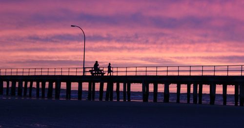 Silhouette people on pier at beach against sky during sunset