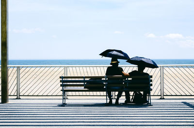 Couple sitting on bench against sky