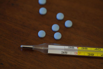 High angle view of thermometer and medicines on wooden table