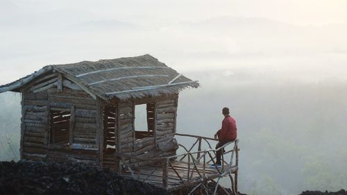 Rear view of man standing by house against sky