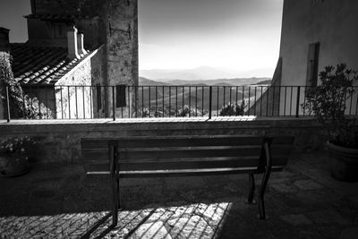 Empty benches and table by buildings against sky