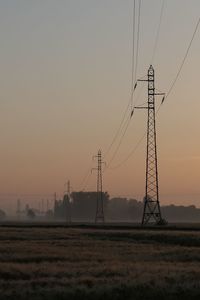 Electricity pylons on field against sky during sunset