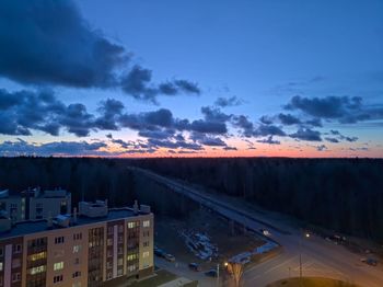 Road by illuminated buildings against sky during sunset