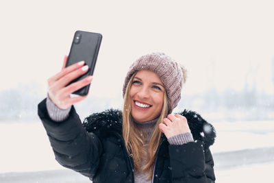 Portrait of smiling young woman using smart phone during winter