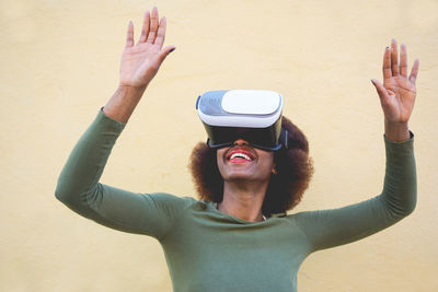 Smiling woman wearing virtual reality simulator against wall