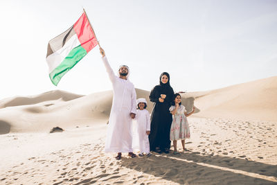 Happy family with united arab emirates flag standing on sand dune