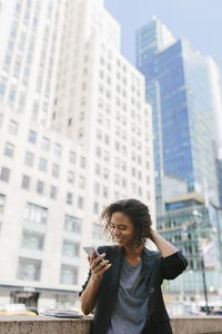 Full length of man using mobile phone against buildings in city