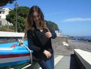 Beautiful woman laughing by boats at beach against sky