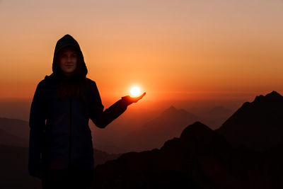 Silhouette man standing on mountain against orange sky