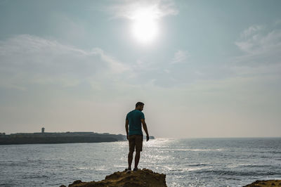 Rear view of man standing at beach against sky