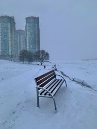 Empty bench against snow and clear sky