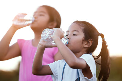 Girls drinking water while standing against sky