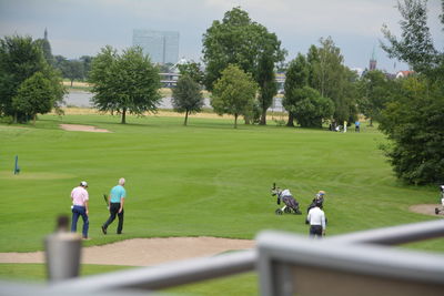 People at golf course against trees