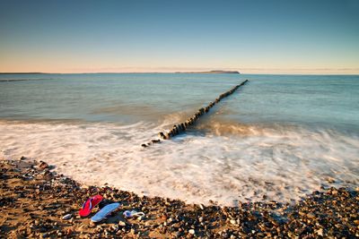 Flip flops and white swimming goggles ready on stony beach at wooden breakwater. wavy sea level.