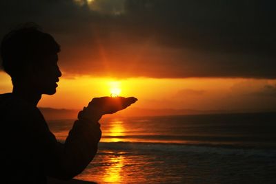 Optical illusion of man holding sun by sea during sunset