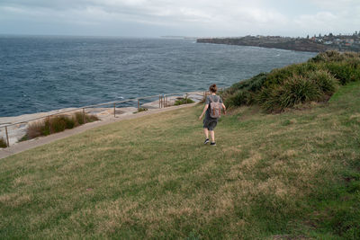 Full length of woman walking on grass towards sea