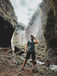 Full length of man standing on rock against waterfall