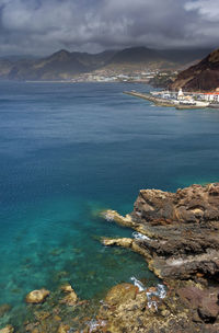 Scenic view of sea by mountains against cloudy sky