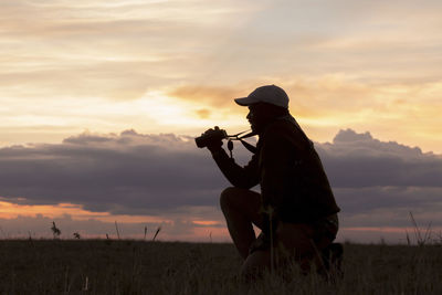Side view man kneeling on field at serengeti national park during sunset