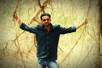 Portrait of young man with arms raised standing in forest