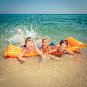 Portrait of children splashing water while lying on pool raft at seashore