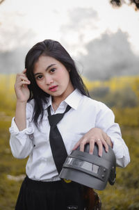 Portrait of young woman wearing shirt and tie holding helmet on land