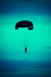 Silhouette person paragliding against blue sky