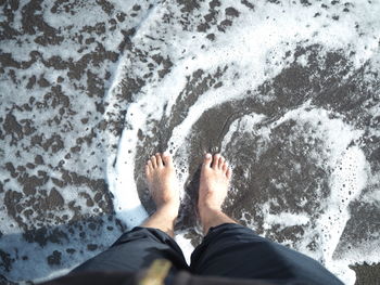 Low section of man standing on wet shore