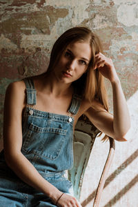 Portrait of young woman sitting on chair against wall