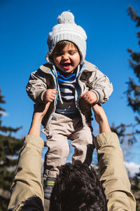 Low angle view of man holding up baby against clear sky