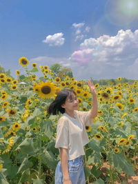 Woman standing by yellow flowers on field against sky sunflower garden 