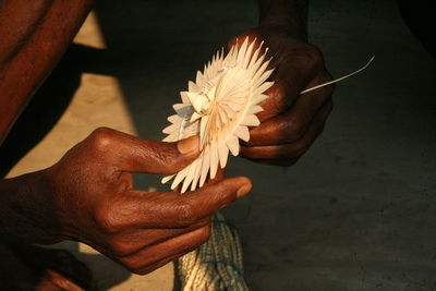 Cropped hand of a man holding a flower made of palm leaves