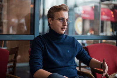 Young man with blonde hair and spectacles looking away while sitting in cafe