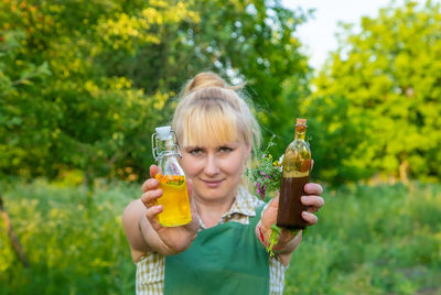 Young woman drinking glass bottle against trees