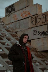 Young man in warm clothes standing against wall