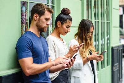 Friends using phones while standing against wall