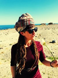 Young woman wearing sunglasses on beach against clear sky