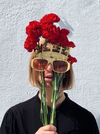 Portrait of woman holding red flower against white wall