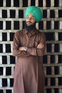 Portrait of young man standing with arms crossed against wall