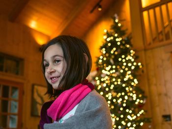 Smiling girl standing against illuminated christmas tree at home
