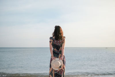 Rear view of woman standing in sea against sky