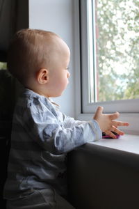 Boy looking away while sitting on window at home