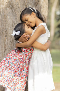 Side view of sisters embracing while standing outdoors