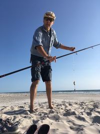 Low angle view portrait of man holding fishing rod standing at beach against sky
